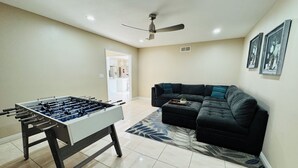 Un salon avec une table de baby-foot, un canapé d’angle et un ventilateur de plafond.