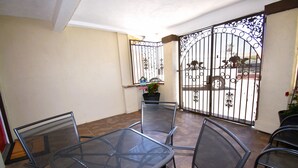 Une terrasse avec une table et des chaises en métal, un pot de fleurs et un portail décoratif.