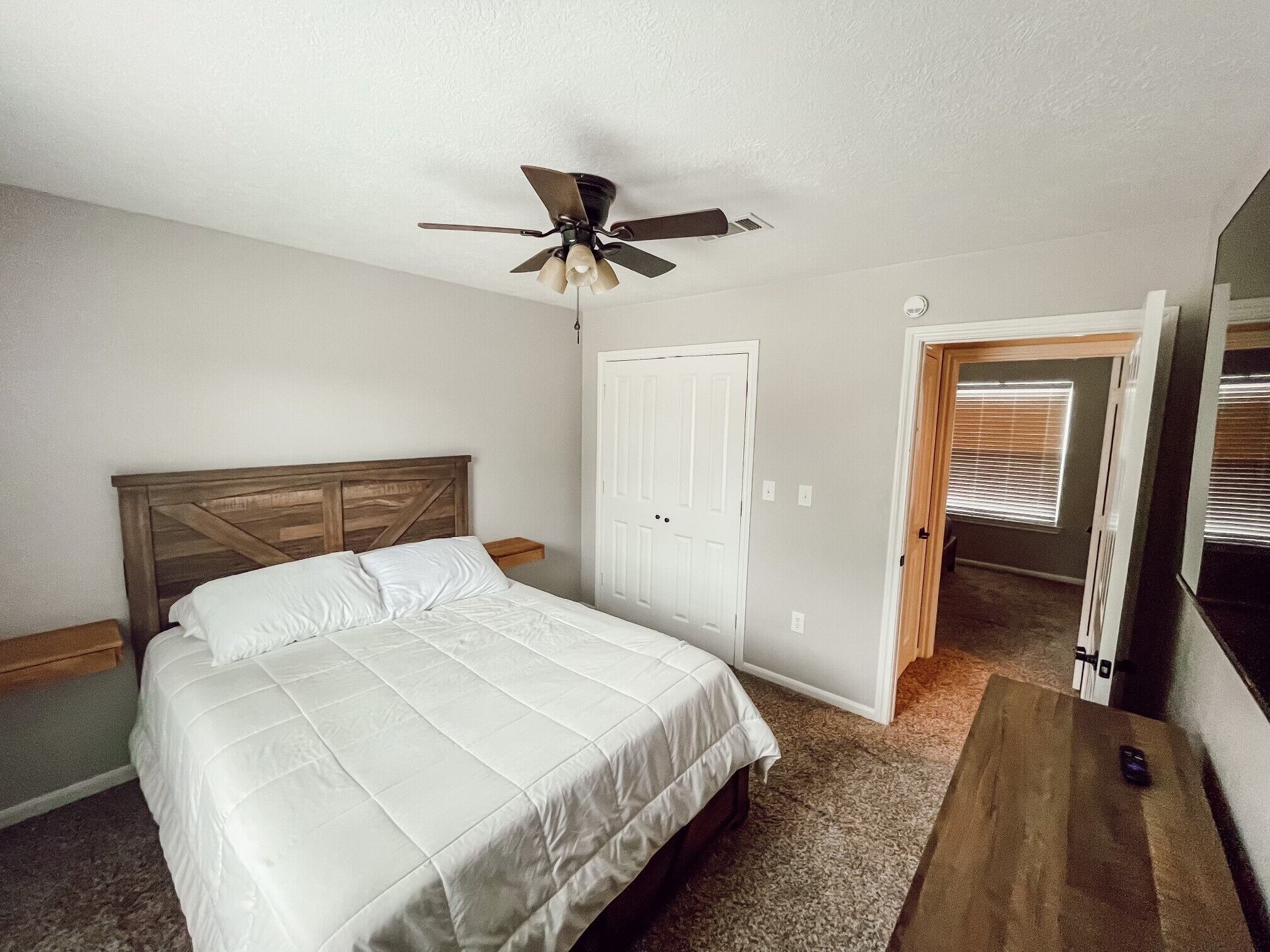 Une chambre à coucher avec un lit, un ventilateur de plafond, une porte et une fenêtre avec des stores.
