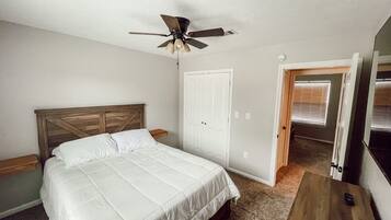 Une chambre à coucher avec un lit, un ventilateur de plafond, une porte et une fenêtre avec des stores.