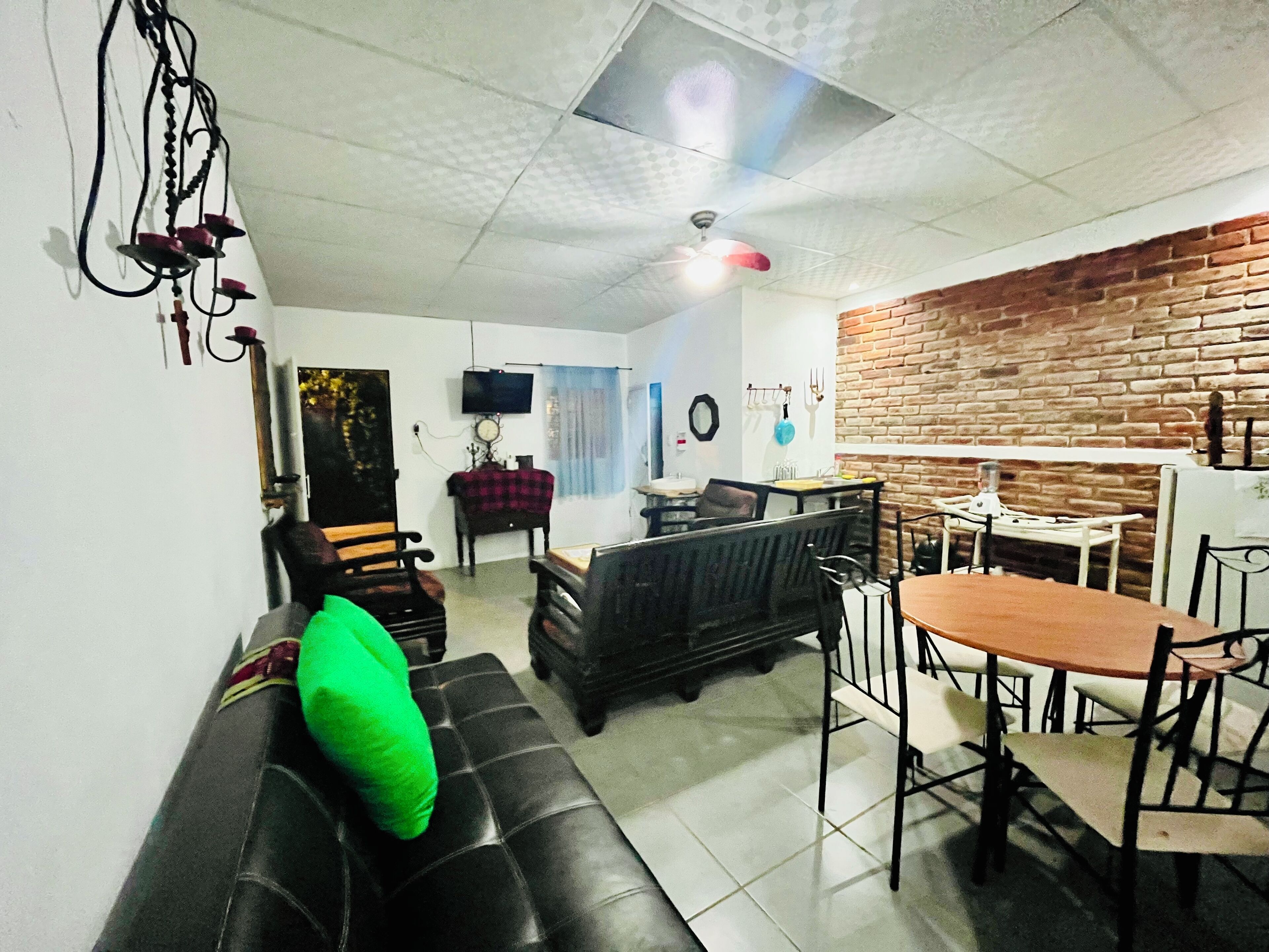 Ein Wohnzimmer mit einer schwarzen Ledersofa, einem Esstisch mit Stühlen, einer Ziegelwand und einem Deckenventilator.