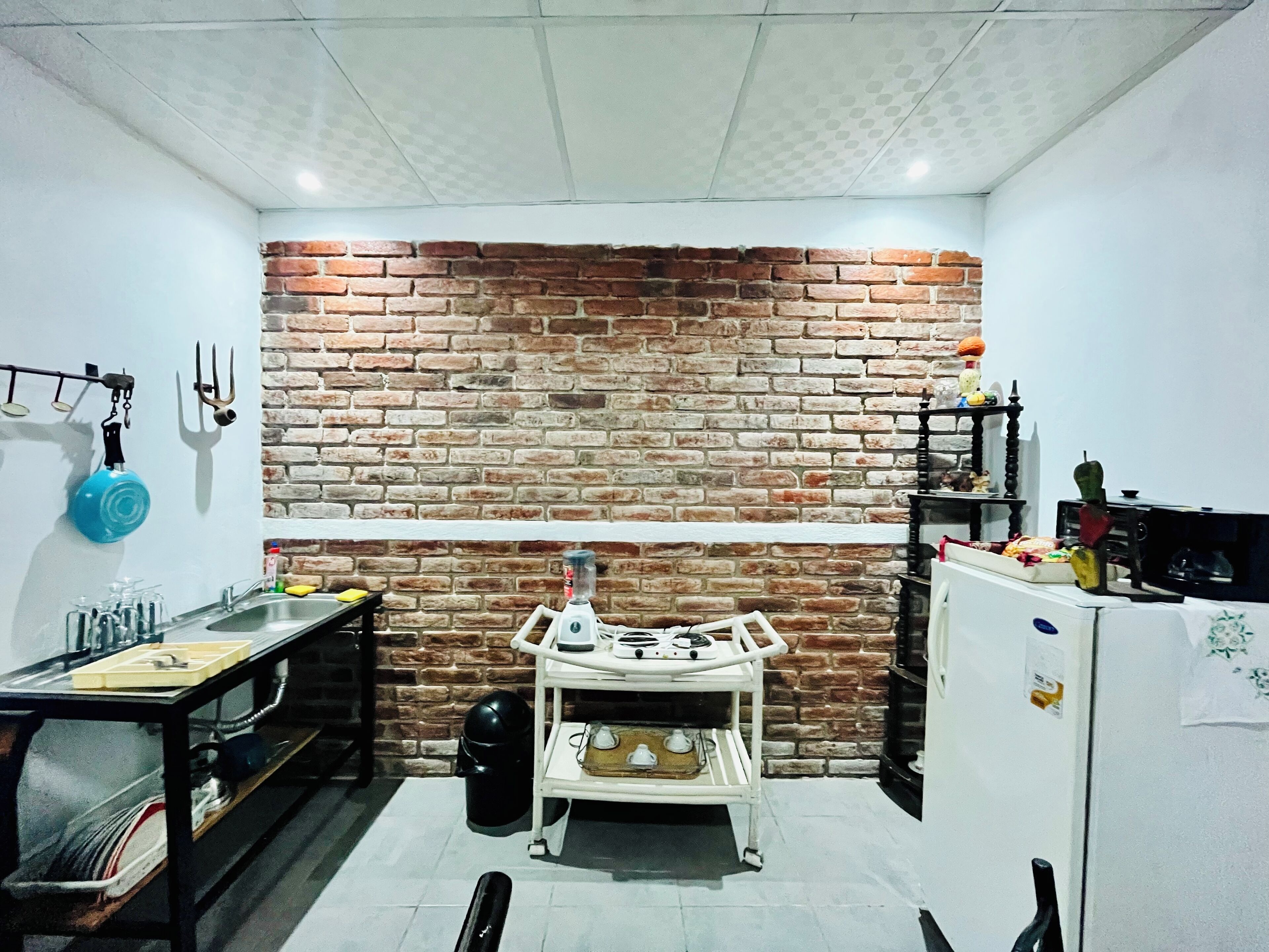 A kitchen with a brick wall, a gas stove, a sink, and a small table with various kitchen items.