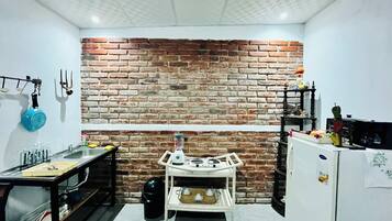 A kitchen with a brick wall, a gas stove, a sink, and a small table with various kitchen items.