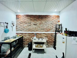 A kitchen with a brick wall, a gas stove, a sink, and a small table with various kitchen items. - Entre Tejas 1 (Concepción de Ataco)