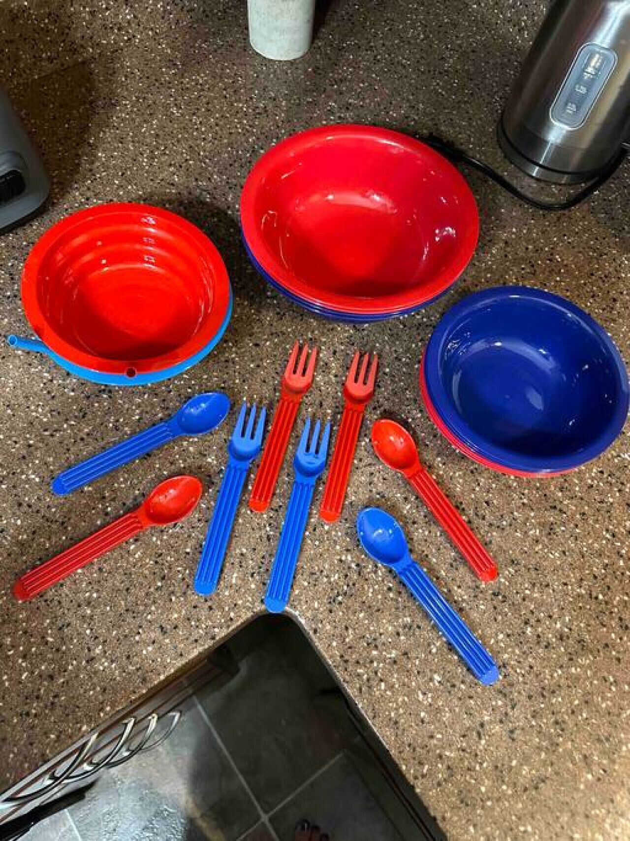 A kitchen counter with red and blue dinnerware, including plates, bowls, and utensils.