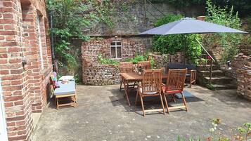 Eine Ziegelterrasse mit Tisch und Stühlen, umgeben von Grünpflanzen und einer Steinmauer.