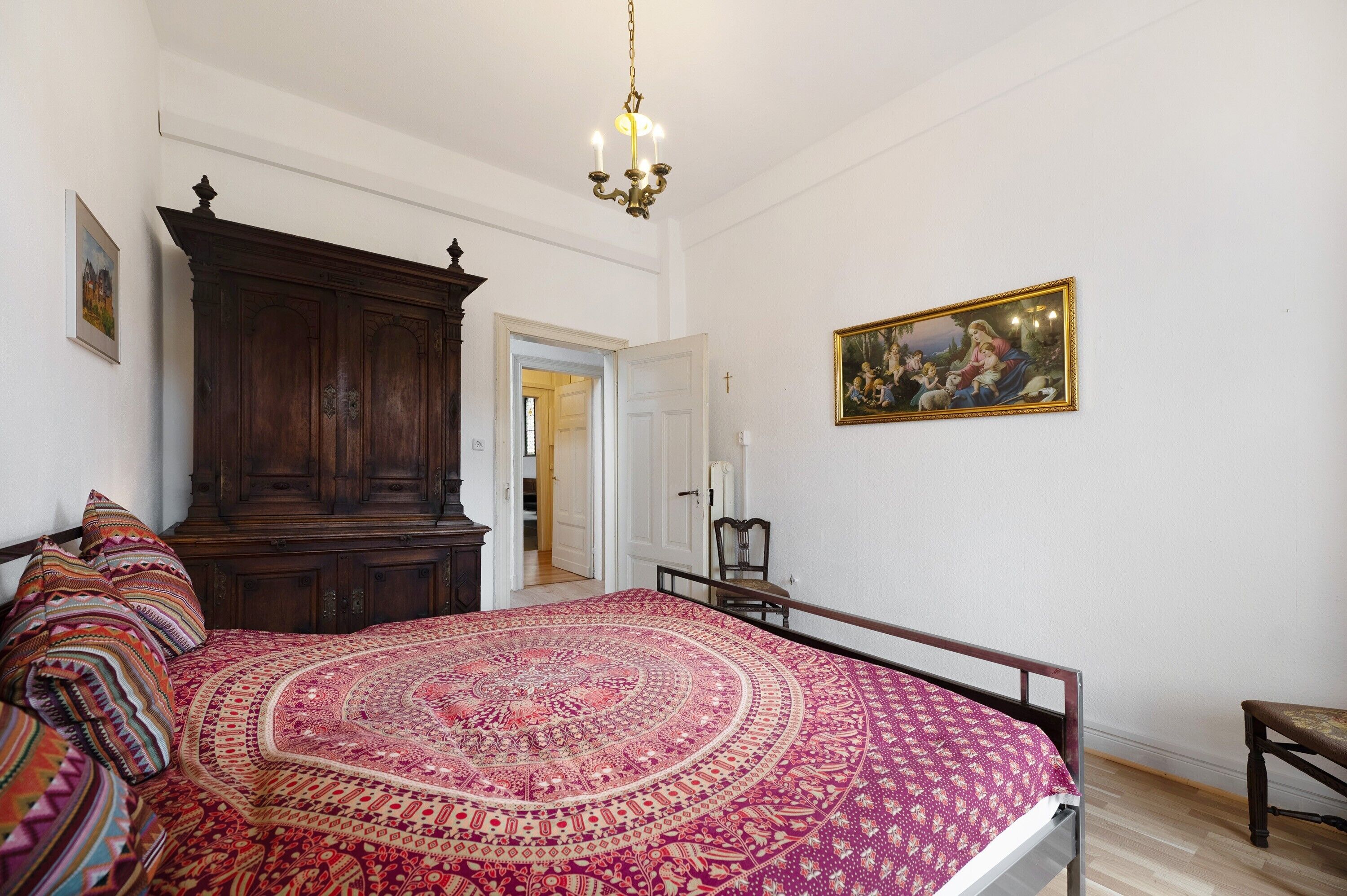 Un dormitorio con una cama grande, un armario de madera, un cuadro en la pared y una araña.