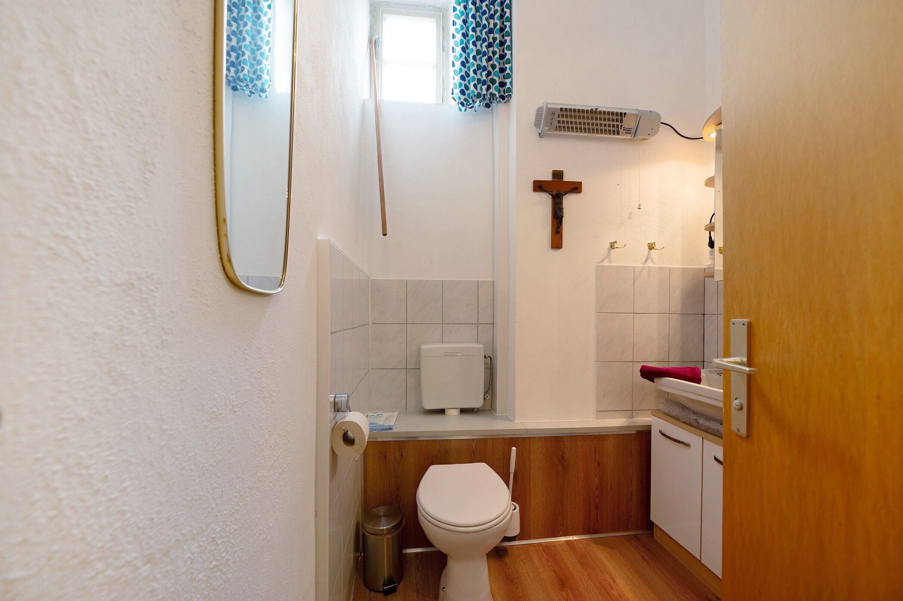 A small bathroom with a toilet, a hand dryer, a trash bin, a towel rack, and a wooden door.
