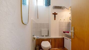 A small bathroom with a toilet, a hand dryer, a trash bin, a towel rack, and a wooden door.