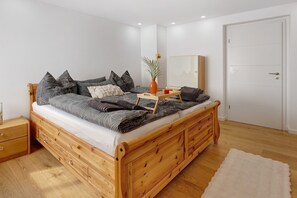 A wooden bed with storage drawers, a bedside table, a mirror, and a white door.