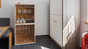 Une pièce avec un meuble en bois doté de portes en verre, un canapé gris et une valise rouge.