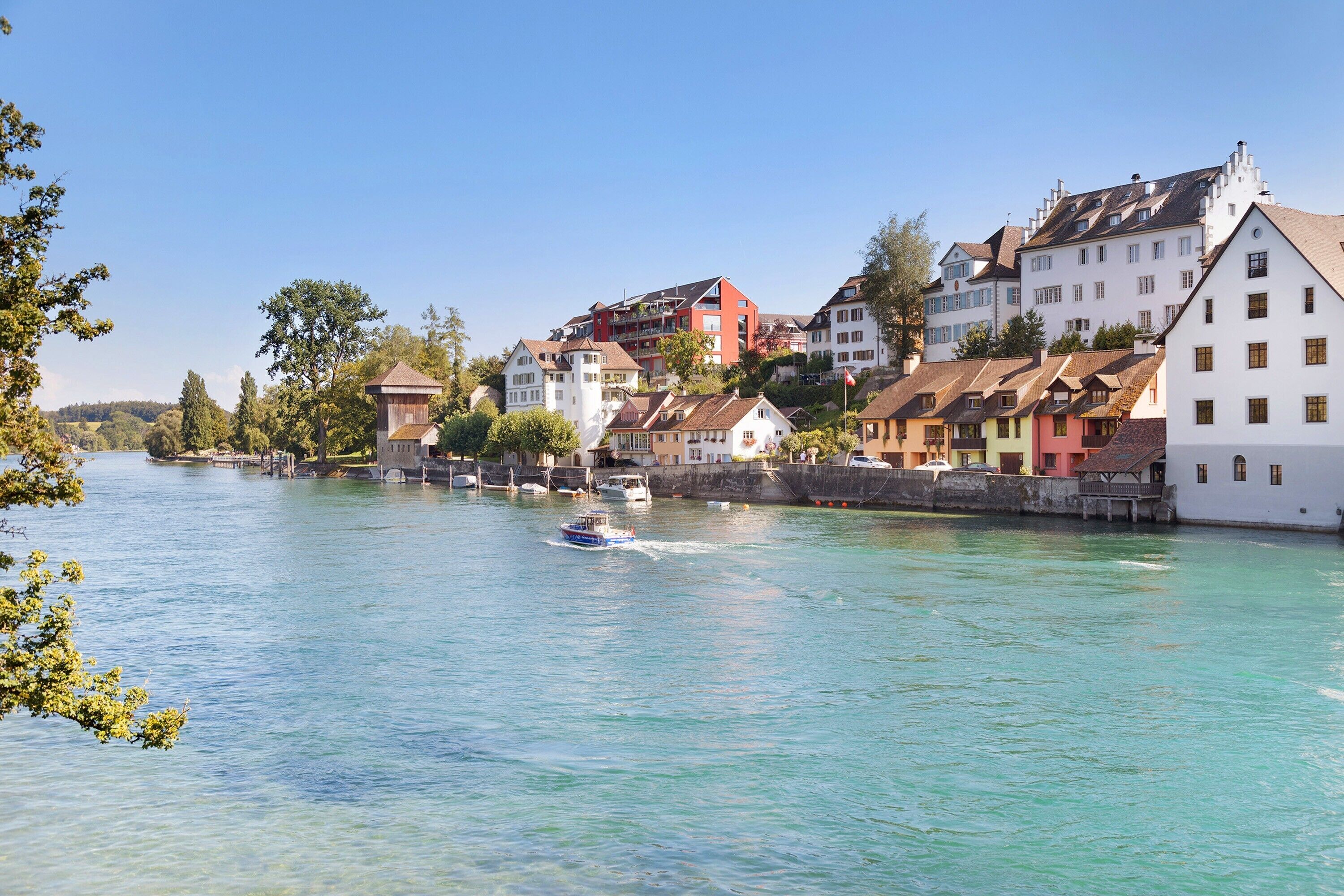 A river with buildings along the banks, a boat on the water, and a clear sky.