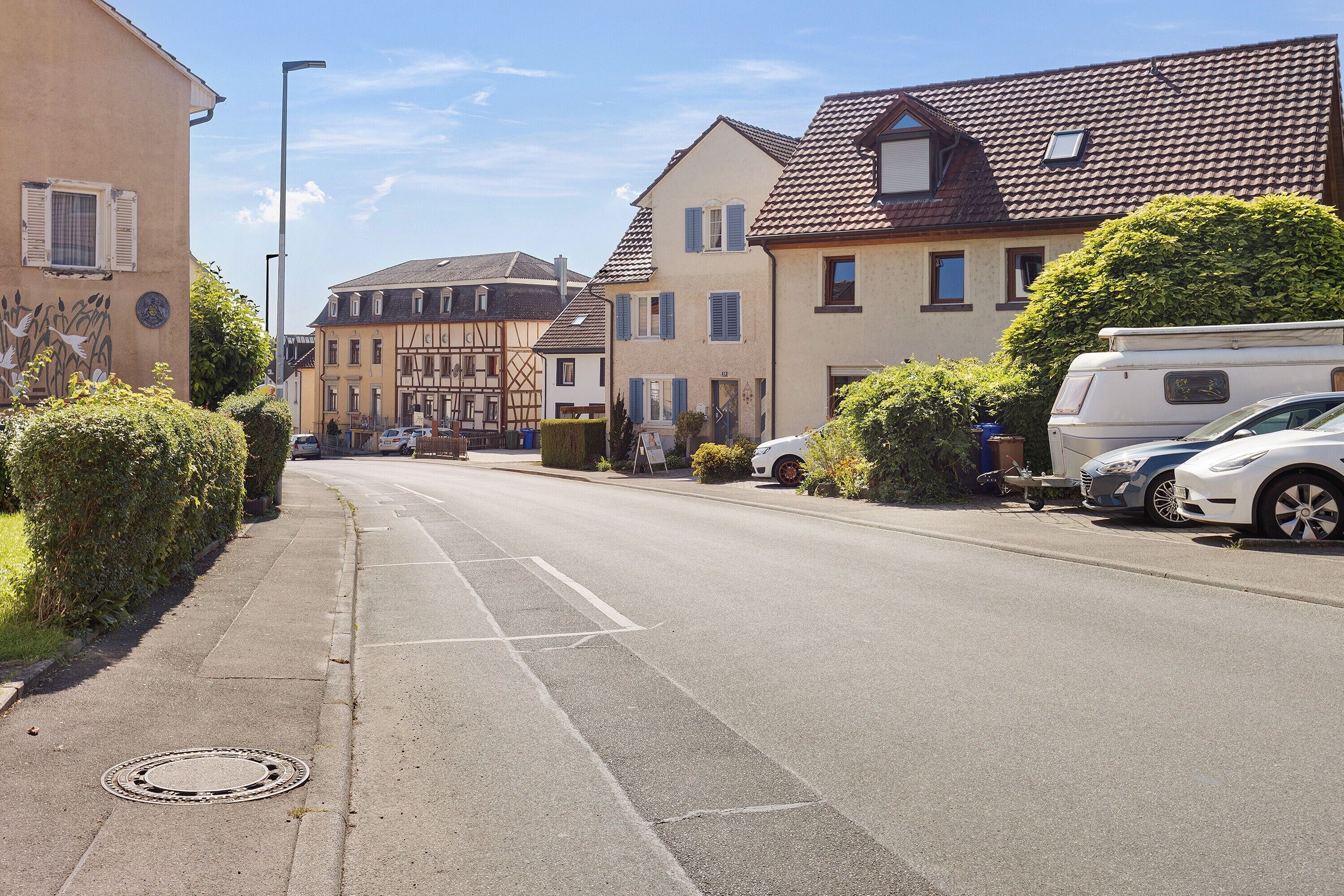 A residential street with houses, parked cars, and a manhole cover.