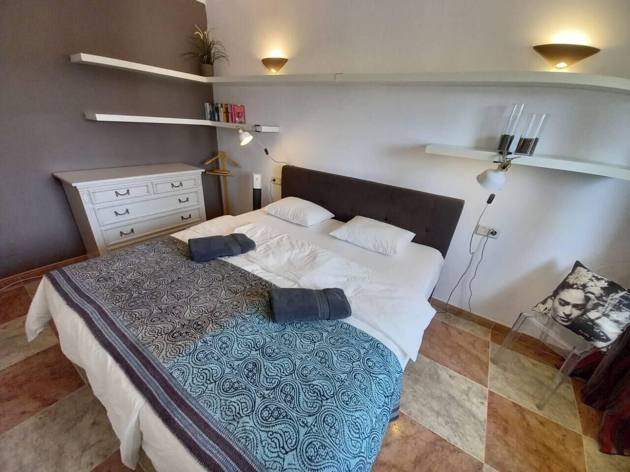 Une chambre à coucher comprenant un lit, des tables de chevet, une commode et des étagères murales.
