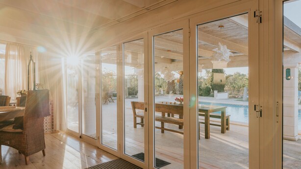 Une pièce spacieuse dotée de grandes portes-fenêtres coulissantes qui donnent sur un patio extérieur avec une piscine, des meubles en bois et une pergola.