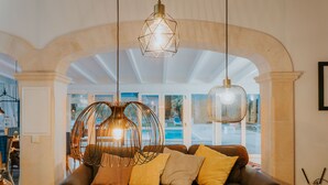 Un salon chaleureux avec un canapé en cuir marron, des coussins jaunes et blancs, et une grande fenêtre donnant sur la rue.