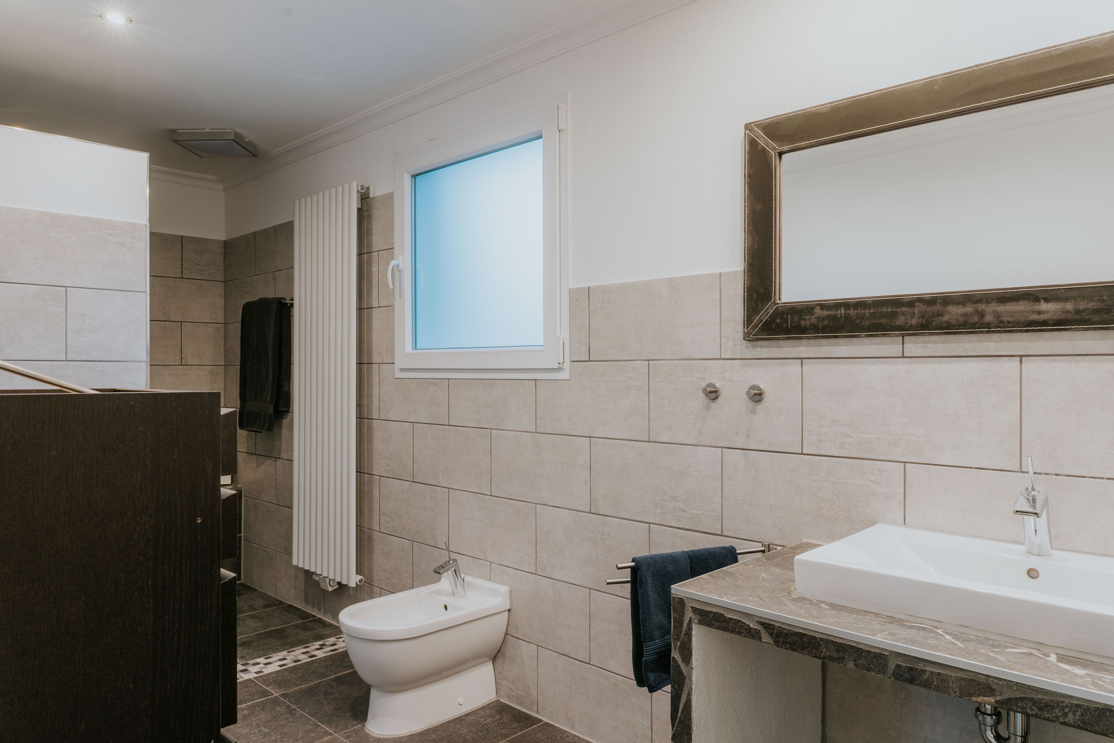 A modern bathroom with a toilet, bidet, and a large mirror above a sink.