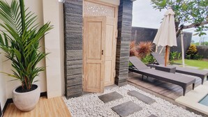 A modern outdoor area with a potted plant, a wooden door, a lounge chair, and a pool.