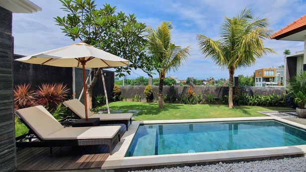 A swimming pool with lounge chairs and an umbrella, surrounded by a well-maintained lawn and palm trees.