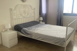 Una cama individual con cabecera de metal, una mesita de noche con lámpara y una mesita auxiliar con lámpara.