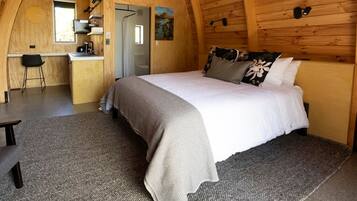 Cozy cabin room with a large bed, compact kitchenette, and wooden paneling.