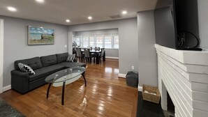 A modern living room with a sofa, glass coffee table, fireplace, and dining area with chairs and a table.