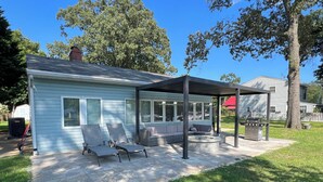 A covered patio with seating and a grill area, surrounded by a well-maintained lawn and trees.