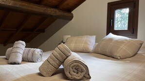 A bedroom with a wooden ceiling, a window, and a bed with beige bedding and rolled towels. - Casa Rural Independiente en Asturias, Admitimos Mascotas (Llanuces)