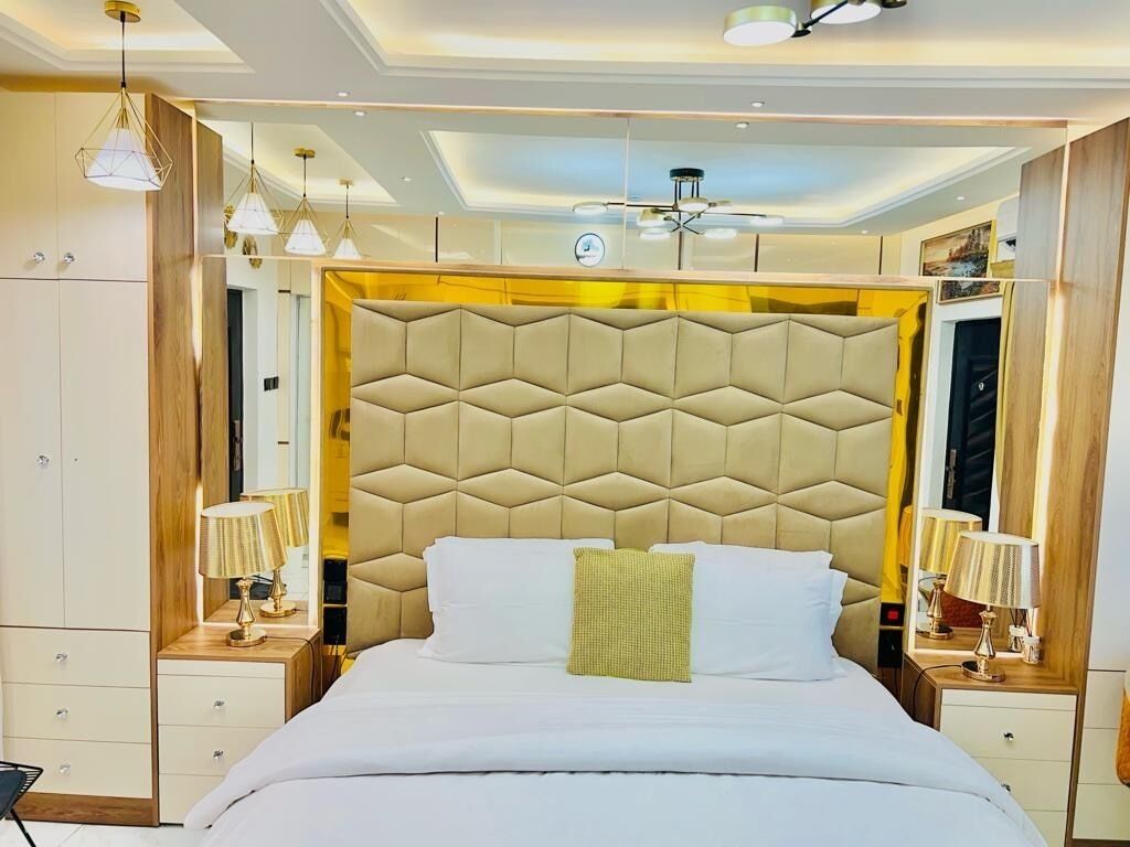 Un dormitorio moderno con un cabecero capitonado, mesitas de noche con lámparas y un ventilador de techo.