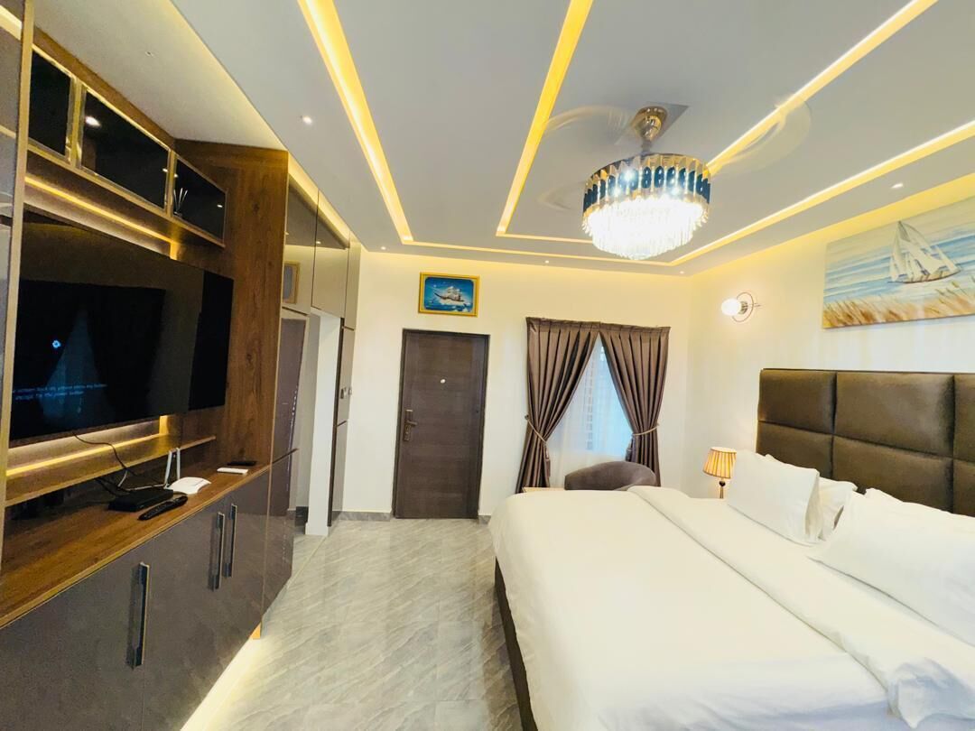 A modern hotel room with a large bed, a television, a chandelier, and a painting on the wall.