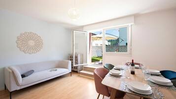 Ein modernes Wohnzimmer mit einer Couch, einem Esstisch für vier Personen und einem großen Fenster mit Blick auf einen Garten.