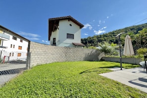 Um bairro residencial com uma pequena casa branca, uma parede de tijolos e um gramado.