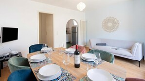 Comedor con mesa de madera dispuesta para cuatro personas, una botella de vino y un sofá blanco al fondo.