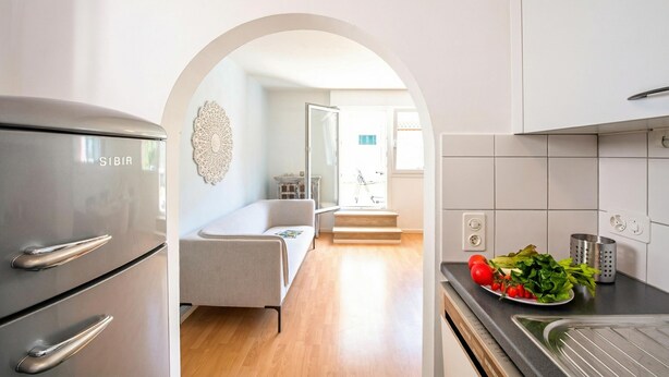Una cocina moderna con un refrigerador de acero inoxidable, un comedor con sofá y vista hacia una sala de estar.