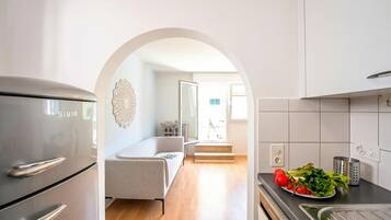 Eine moderne Küche mit einem Edelstahl-Kühlschrank, ein Essbereich mit einer Couch und Blick in ein Wohnzimmer.