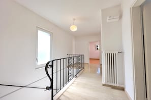 A hallway with a staircase, a radiator, and a door leading to another room.