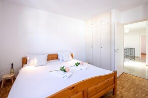 A neatly made bed with white linens, a wooden headboard, and a bedside table with a bottle and glasses.