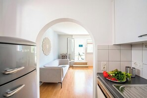 Eine moderne Küche mit einem Edelstahl-Kühlschrank, eine Essecke mit einer Couch und ein Blick in ein Wohnzimmer durch einen Bogen.