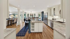 Une cuisine moderne avec des meubles blancs, un îlot central et un réfrigérateur en acier inoxydable.