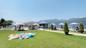 A lakeside park with picnic tables, umbrellas, and a gazebo. - Mansarda Vialba Apartment in Holiday Home with Lake View and Balconies (Germignaga)
