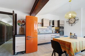 Une cuisine moderne avec un grand réfrigérateur orange, des armoires en bois et un coin repas agrémenté d’une nappe à rayures.