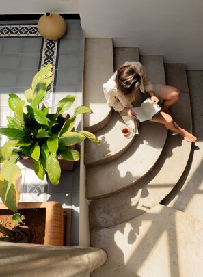 A person reading a book on a curved staircase with a potted plant beside them.