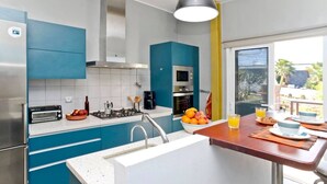 A modern kitchen with a gas stove, oven, and a sink. There is a dining area with a table set for two and a view of the outdoors. - Holiday Villa 'Casa Jenabe' with Mountain Views, Private Terrace and Wi-Fi (la vegueta)