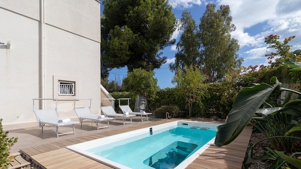 Piscina rectangular con muelle de madera, rodeada de sillas de descanso y follaje.