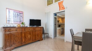 Una sala de estar con un aparador de madera, un televisor de pantalla plana, una mesa de comedor con sillas y una cocina visible a través de un vano abierto.