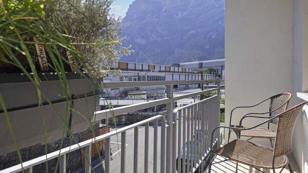 A balcony with a wicker chair, a white railing, and a mountain view.
