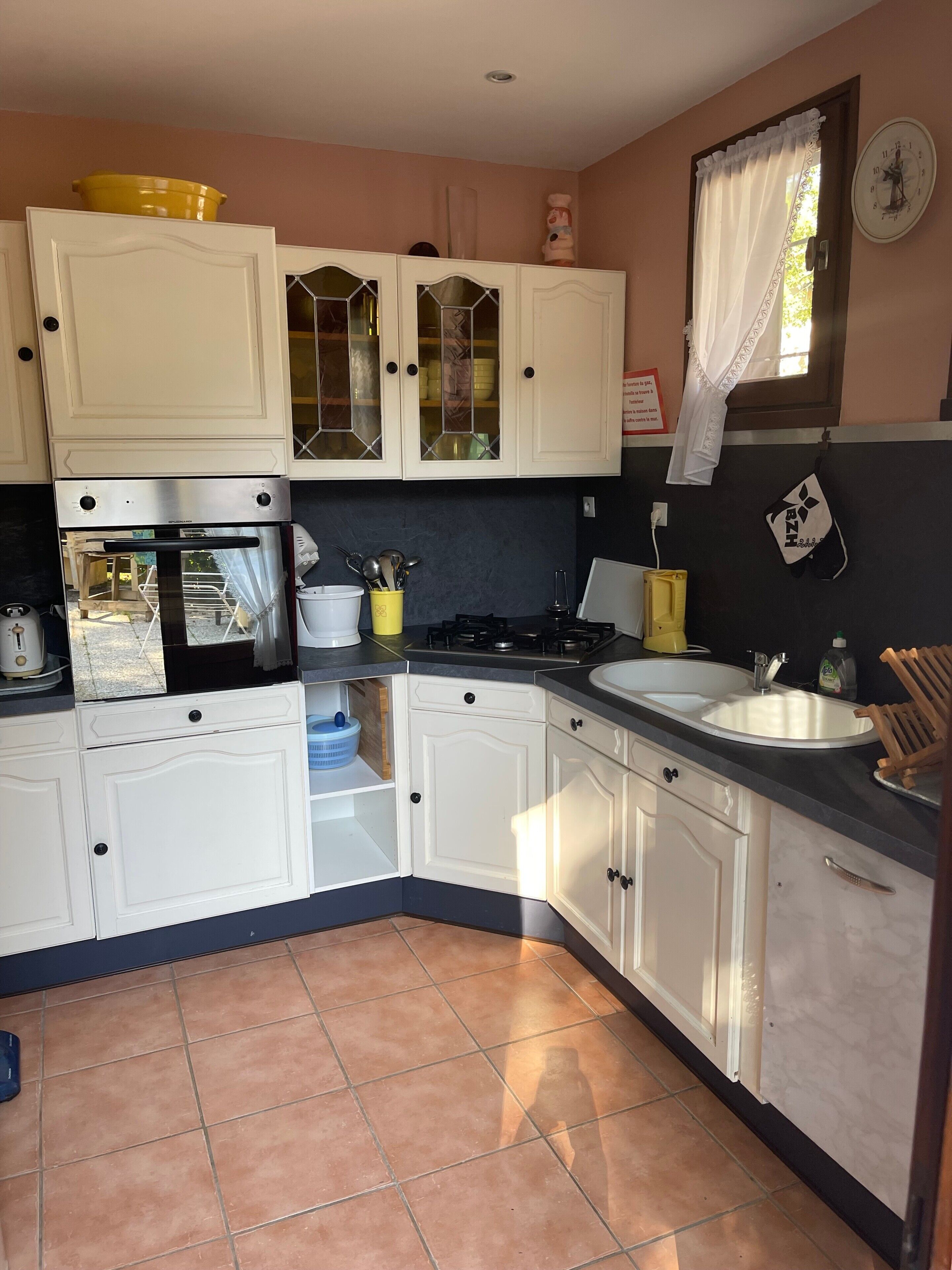 A kitchen with white cabinets, a stove, an oven, a sink, and a window with a curtain.