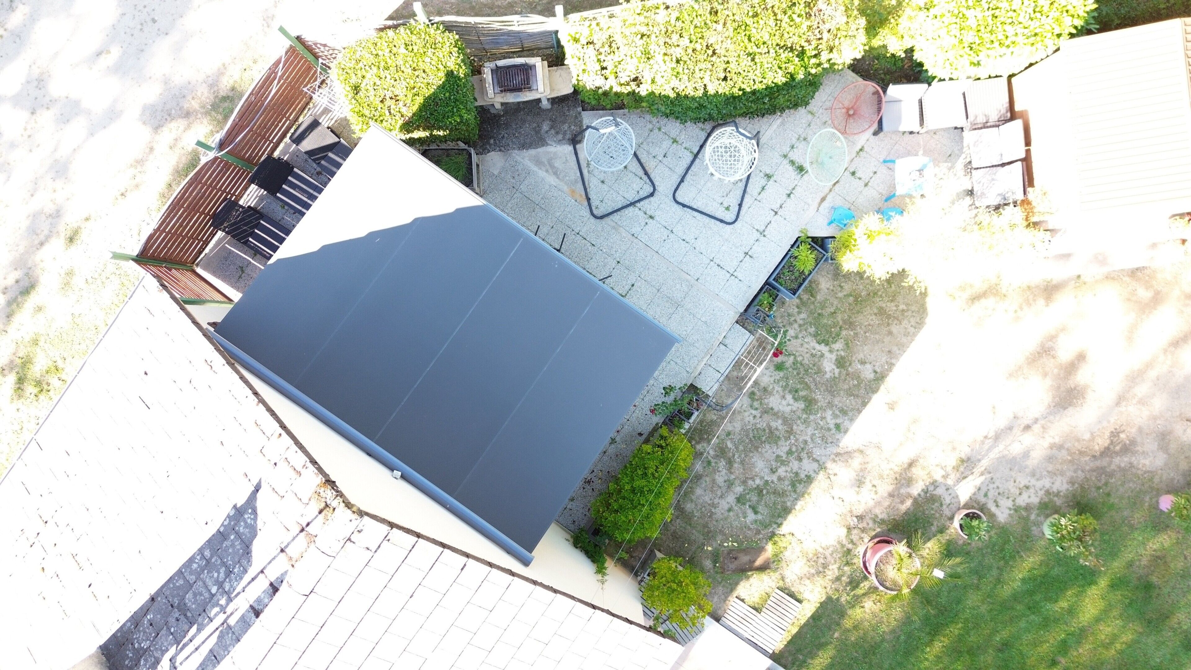 Luftaufnahme einer Dachterrasse mit ebener Fläche, umgeben von Grünpflanzen und einem gepflasterten Bereich mit Gartenmöbeln.