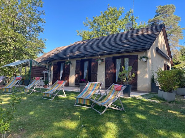 Un petit bâtiment doté d’un toit en pente, de volets en bois et d’un patio couvert avec des chaises longues à rayures.