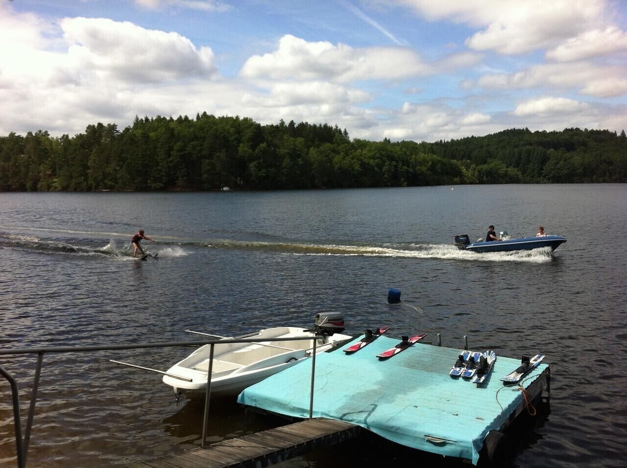 Järvi, jossa on veneitä, laituri ja metsäinen rantaviiva.